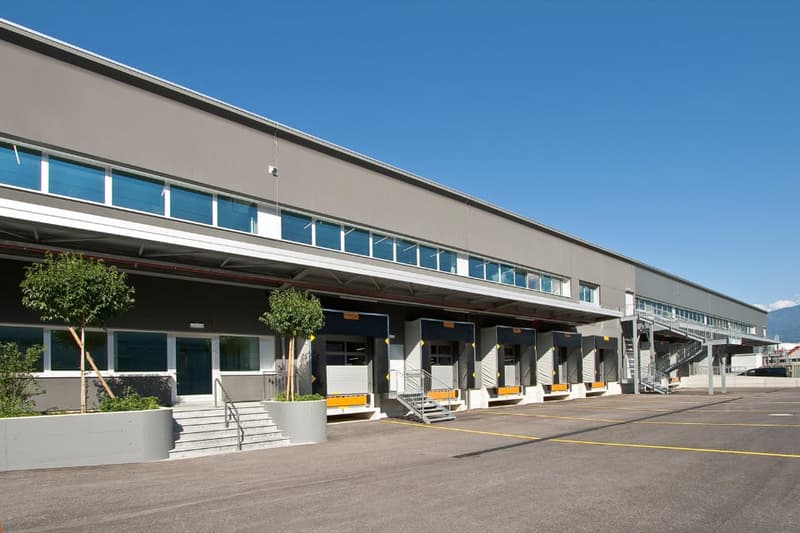 Large commercial building with multiple loading docks, parking spaces, and a modern, minimalist design with gray exterior and large windows