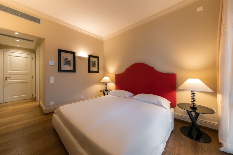 Double bed, red headboard, wooden floor, two nightstands with lamps, decorative picture frames on wall, white walls