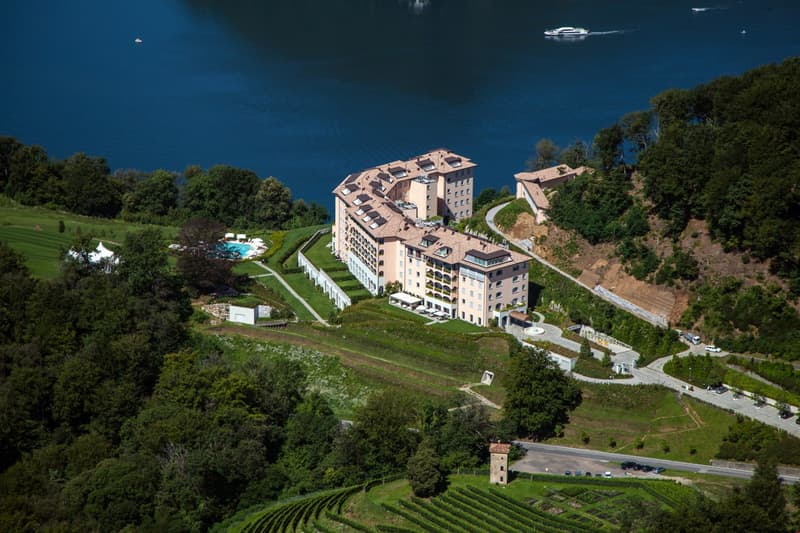 large building with a swimming pool, surrounded by greenery with a scenic lake view