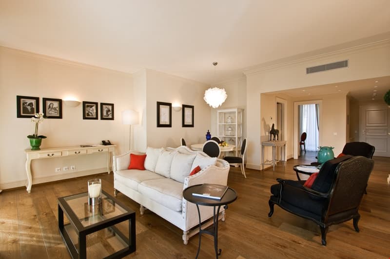 a bright living room with wooden flooring, white sofa, glass coffee table, and black armchairs