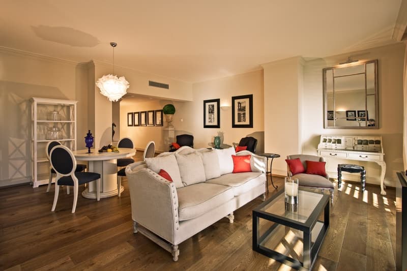 white living room with white and gray couch, white table and chairs, large white cabinet, mirror, lamps