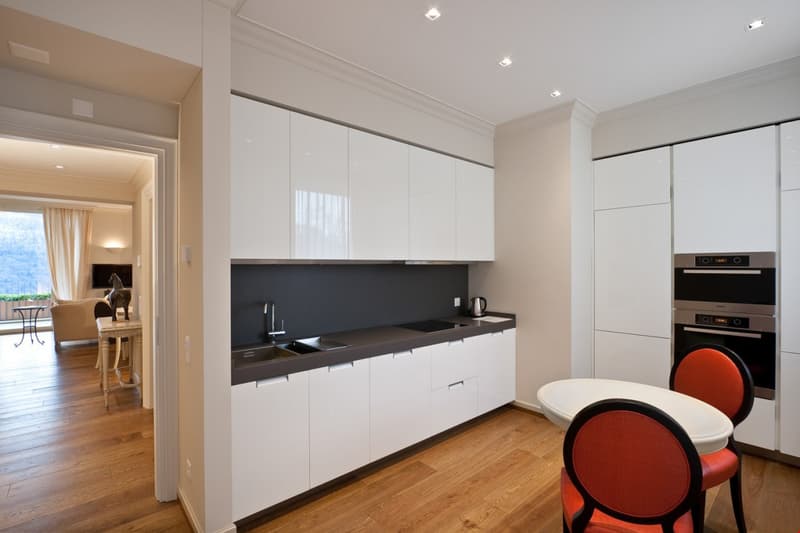 modern kitchen with white cabinetry, marble countertops, integrated dishwasher, large sink, modern faucet, oven, stove, and under-cabinet lighting