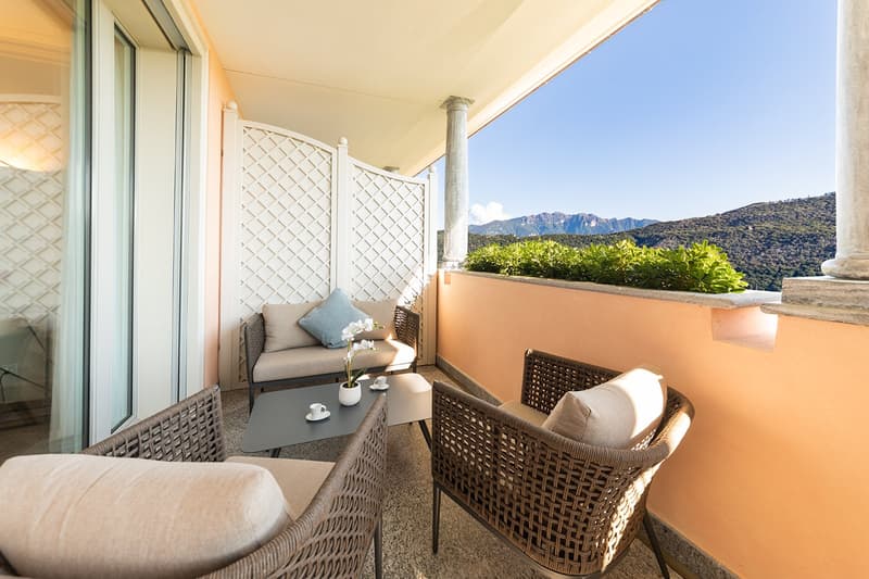 outdoor seating area with table, couch, pillows, flowers, large windows, view of mountains