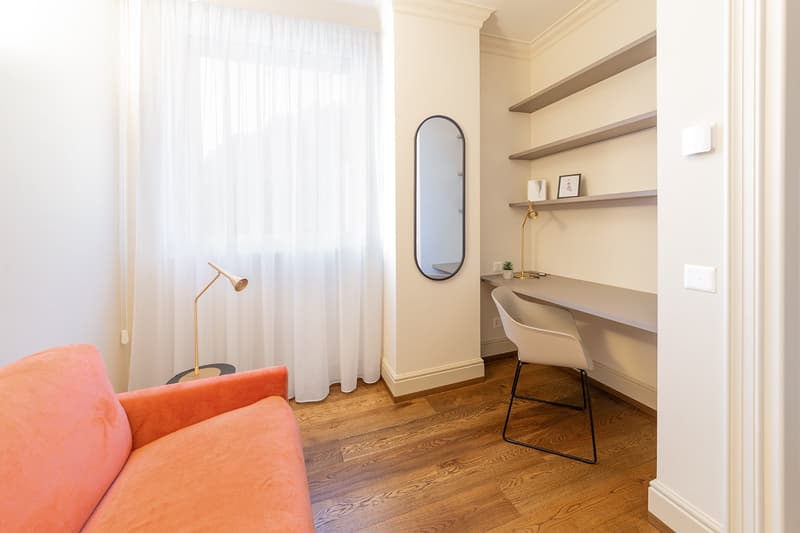 room with an orange couch, white desk, white chair, mirror, lamp, white curtains