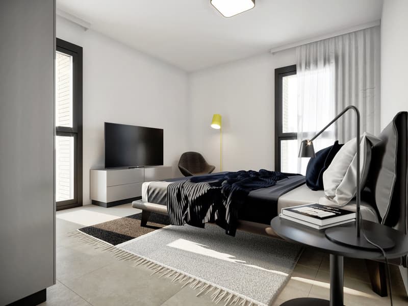 Spacious bedroom with white walls, large windows, hardwood floors, a king-size bed with navy blue bedding, a TV console, and a comfortable armchair.