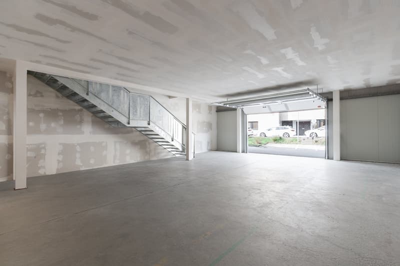 Empty garage with concrete floor, metal staircase, and open garage door.