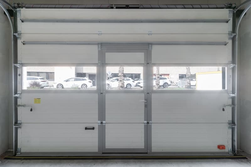 White roll-up garage door with three windows, metal handles, and a yellow sticker