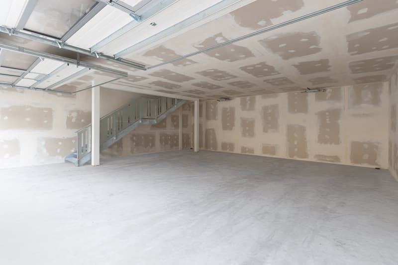 Empty garage with unfinished walls and ceiling, concrete floor, metal stairs