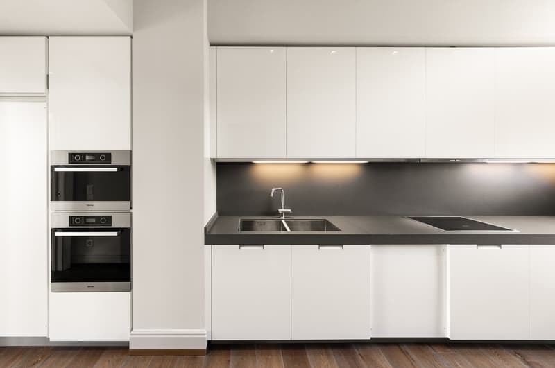 modern kitchen with white cabinets, black countertops, stainless steel sink, induction cooktop, built-in oven, wooden floor