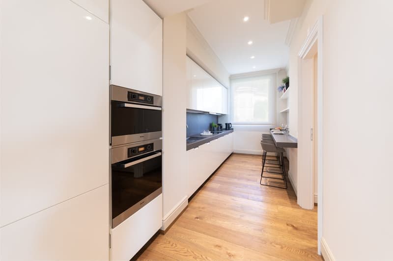 modern kitchen with white cabinets, wooden floor, double oven, dishwasher, bar stools, window