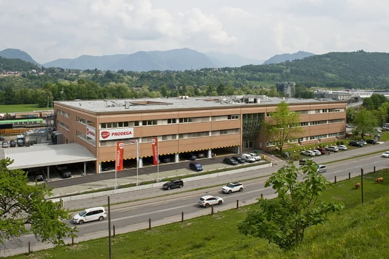 large building, multiple windows, parking lot, cars driving, mountains in the background