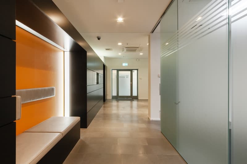 modern office corridor, white ceiling, beige tiles, glass walls, black and orange walls, bench, surveillance camera