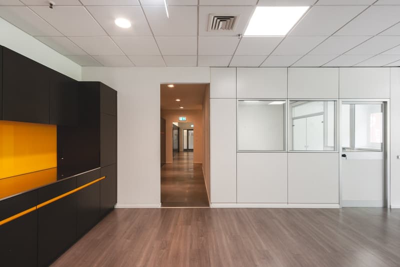 Empty room with wooden floor, white walls, black cabinets, yellow accents, glass doors, and ceiling lights.