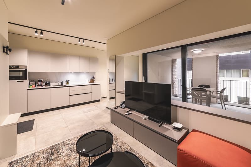 modern kitchen with white cabinets, large windows, balcony, flat screen TV, orange sofa, carpet