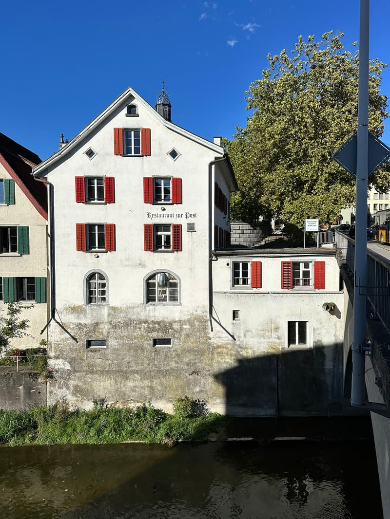 A residential building beside a river, with many windows and red shutters