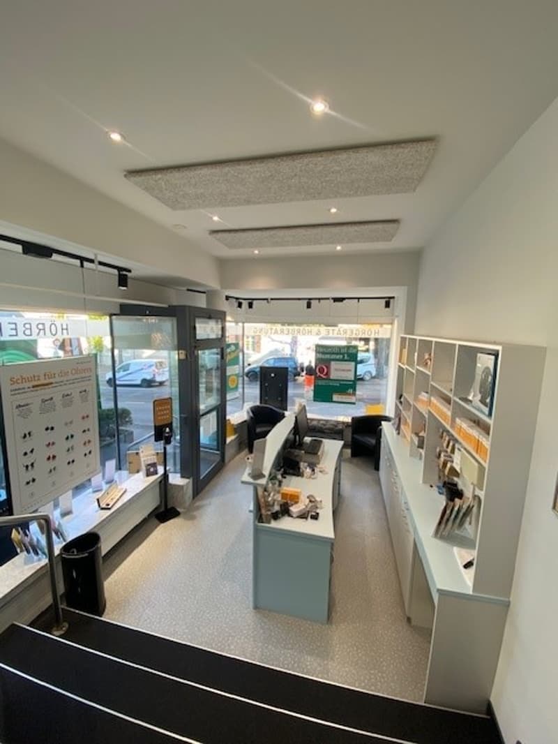 spacious entrance area, minimalist design, large windows, glass doors, counters, cabinets, trash bins, reception desk, display board, indoor lighting, outdoor view
