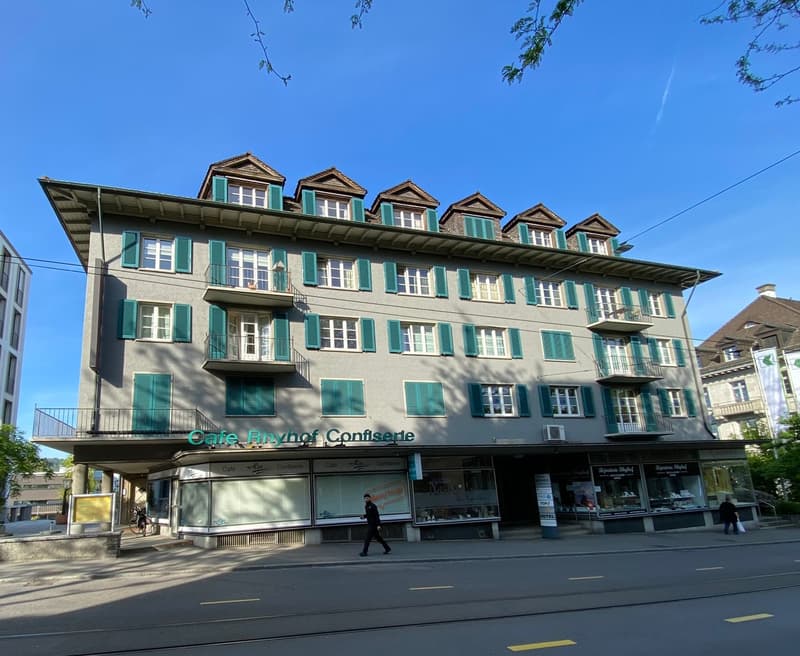 4 story building, grey wall, green shutters, balconies, ground floor cafes