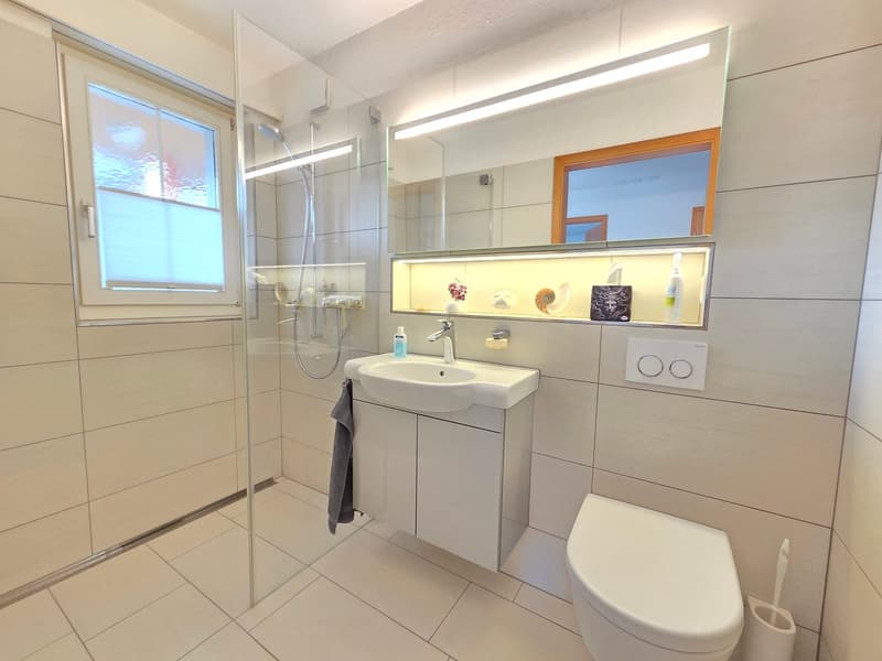 modern bathroom with white tiles, glass walk-in shower, vanity with sink, toilet, and shelves, and overhead lighting