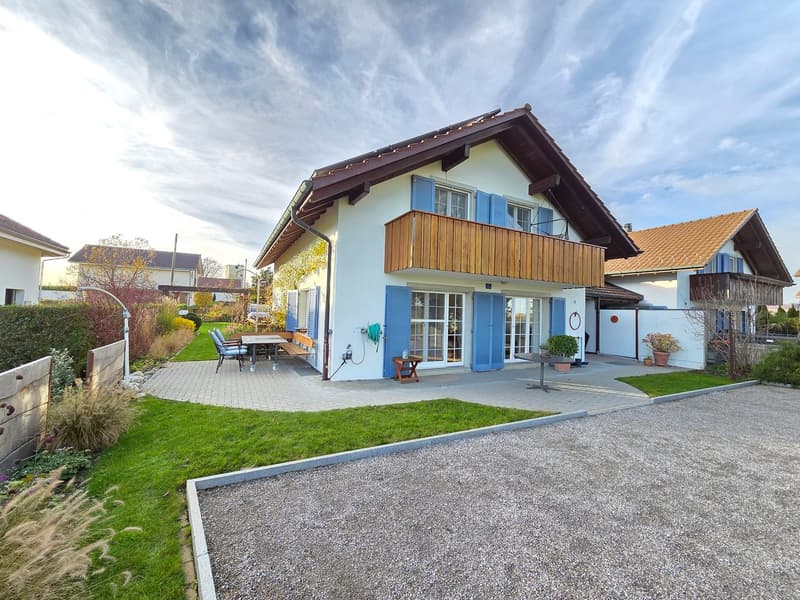 2 story house, white walls, brown roof, blue shutters, wooden balcony, paved patio, garden