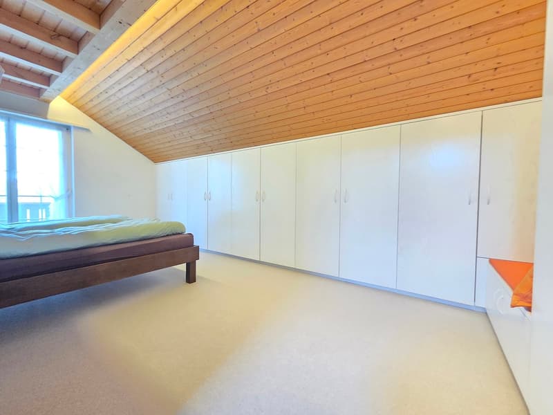 Empty bedroom with wooden ceiling, white walls, carpet floor, white cabinets, and a bed with a mattress and blankets.