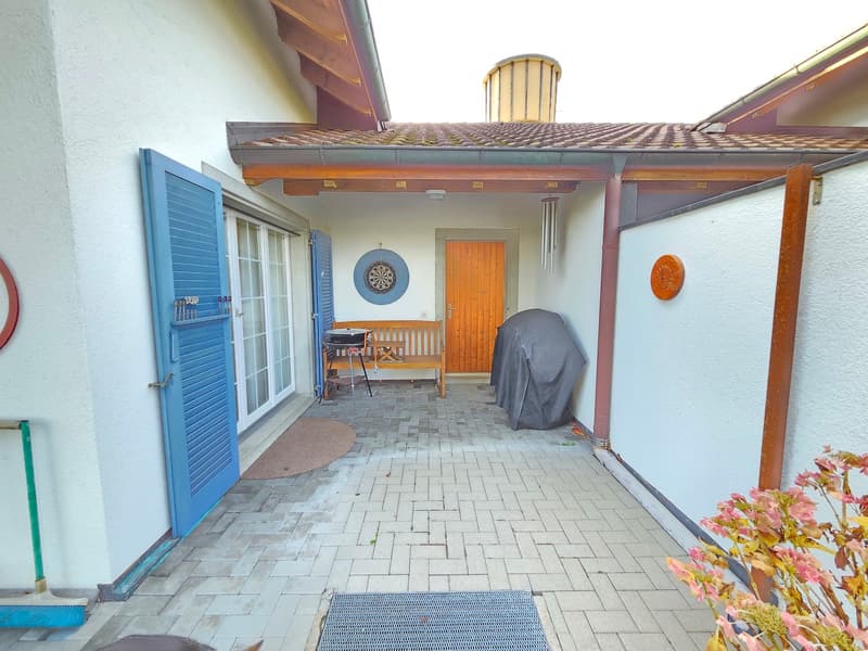 white house, blue shutters, wooden bench, dartboard, covered grill, brick patio
