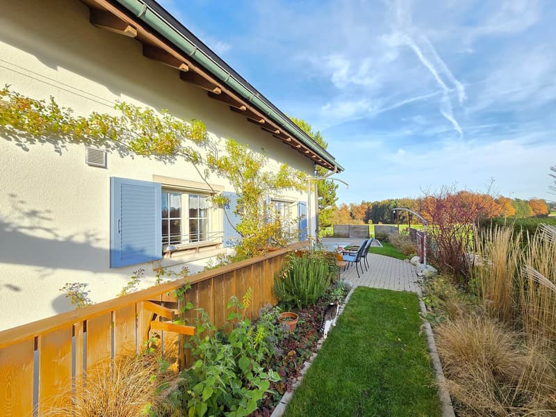 garden with various plants, wooden fence, paved pathway, chairs, and outdoor table