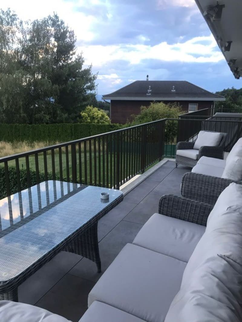 covered balcony with metal railings, black couch with white cushions, metal coffee table, grassy yard, trees