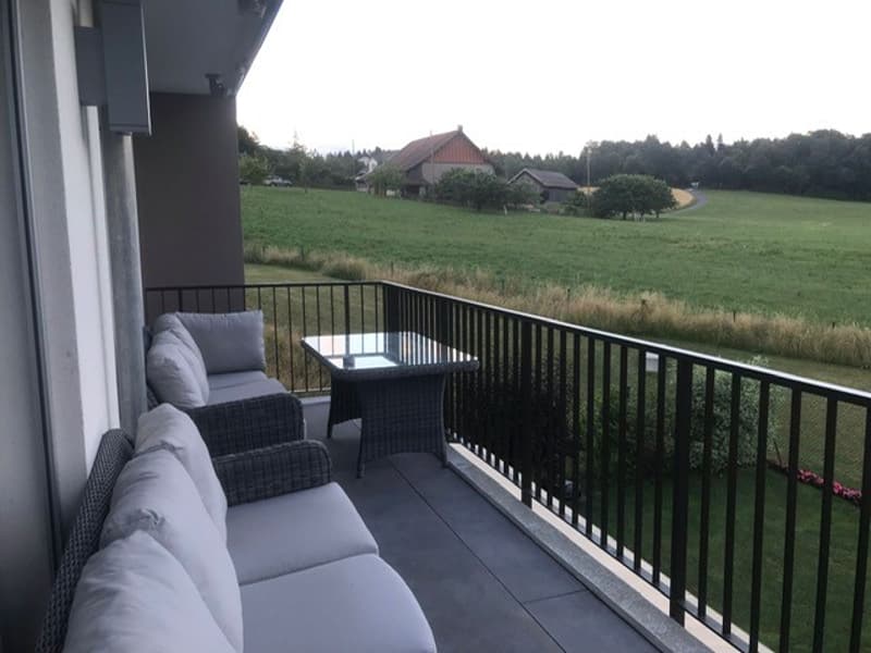 Balcony with seating and table, view of green fields, railings