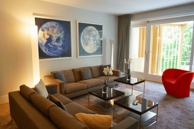 brown couches, two glass tables, artwork, curtains, bright light, glass door leading to balcony