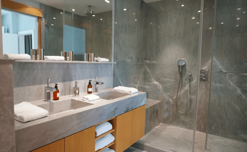 Marble countertops, wooden cabinets, two sinks, large mirror, glass shower, gray tiles