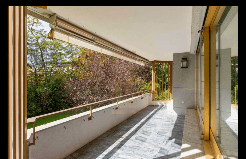 Modern balcony with marble floor, metallic railings, glass doors, wall-mounted light, outdoor vegetation view