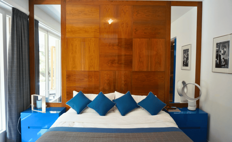 master bedroom with large bed, blue pillows, wooden wall, 2 nightstands, and mirrors