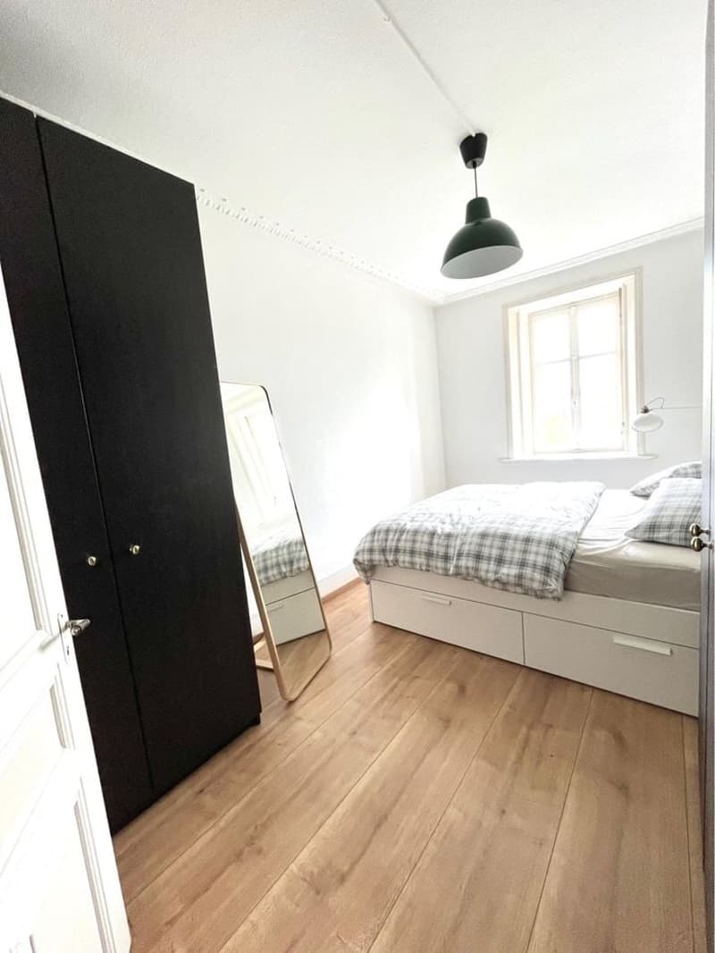Bedroom: Double bed, bedside tables, cabinet, mirror, window, wooden floor, white walls