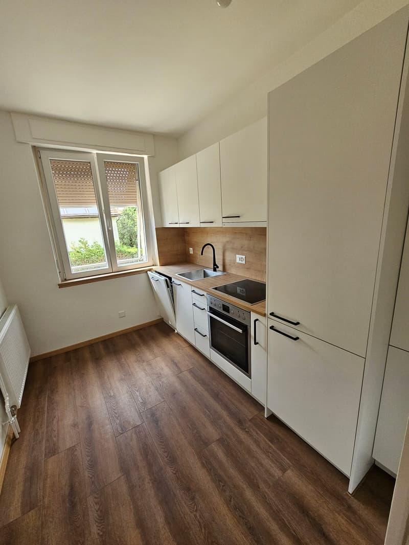 Compact kitchen with white cabinets, wooden countertop, built-in dishwasher, and laminate flooring. Large window providing natural light.