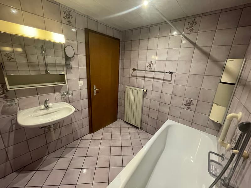 Bathroom with white bathtub, sink, mirror, radiator, and tiled walls