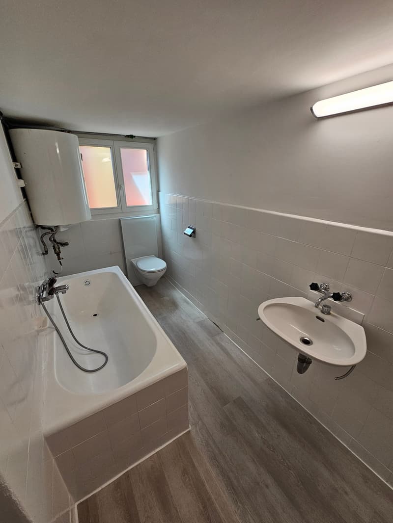 Bathroom with a bathtub, toilet, and sink. The room has tiled walls and a laminate floor.