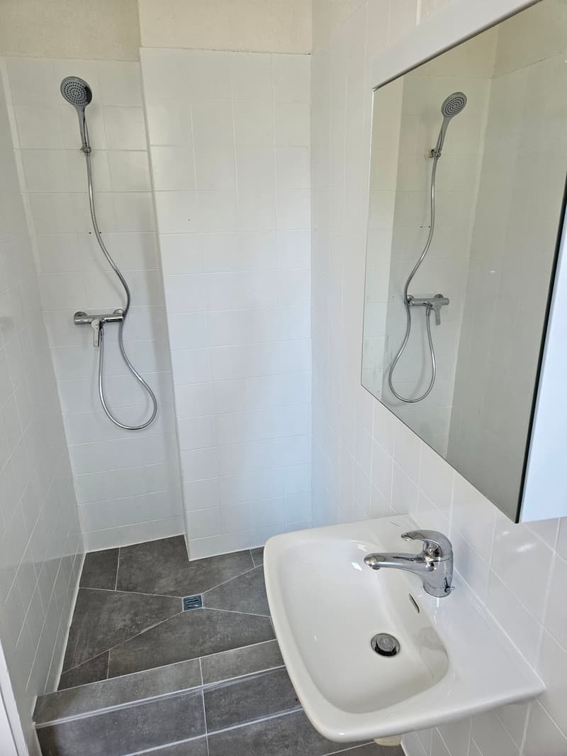 Bathroom with white tiles, two shower heads, a sink, and a floor drain.