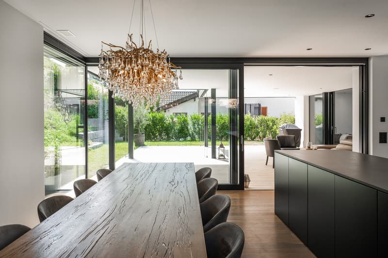 wooden floor, long dining table, modern chandelier, glass doors to terrace, green garden view