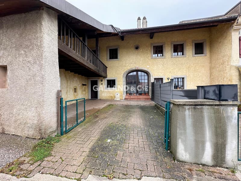 Main entrance with brick flooring, green gates, balcony on the upper floor, beige wall, multiple windows, tiled roof