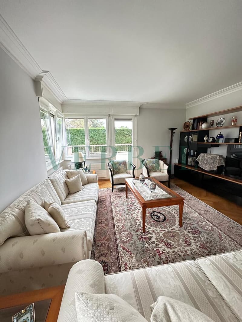 / a living room with a large window, a white couch, a coffee table, and a rug