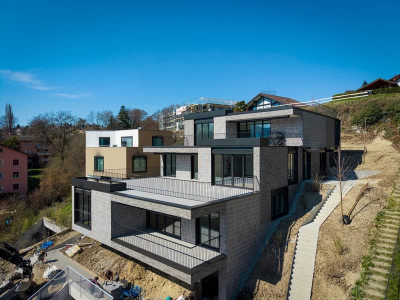 Modern house, multiple levels, balconies, gray brick, glass windows, under construction