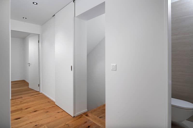 minimalist room with white walls, wooden floor, white sliding door, white toilet, white switch