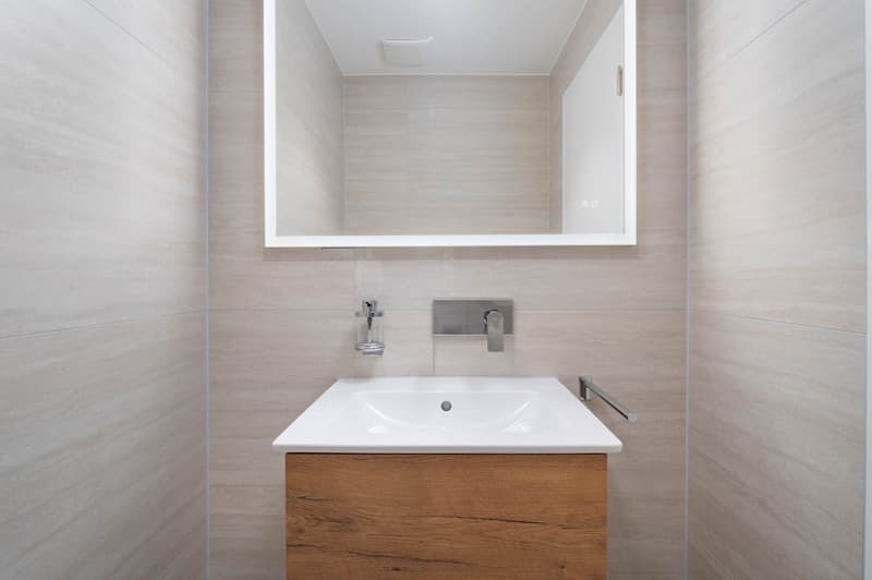 Bathroom with white sink, wooden cabinet, mirror, and tiled walls