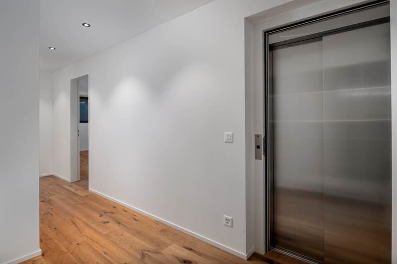 Empty room with white walls, wooden floor, and an elevator