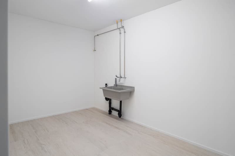 Empty room with white walls, tiled floor, and a wall-mounted sink with a faucet.