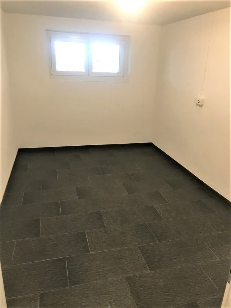 Empty room with white walls, black tiled floor, single window, no furniture.
