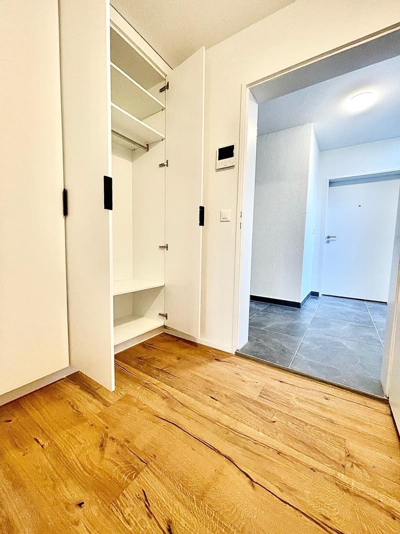 Empty room with wooden floor, white walls, large closet, and an open door leading to another room