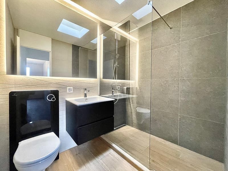 modern bathroom with gray tiles, glass shower enclosure, white toilet, black vanity with sink, wooden floor