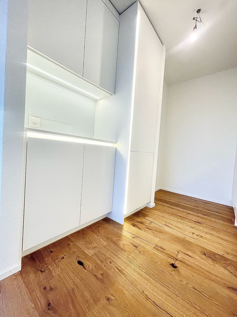 Empty room with white walls, wooden floor, white cabinets, and ceiling light