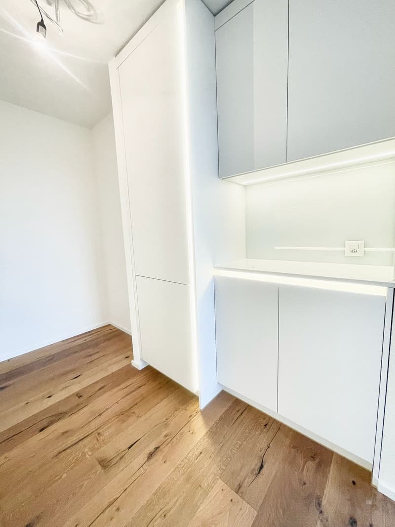 Empty room with white walls, wooden floor, white cabinets, and ceiling light